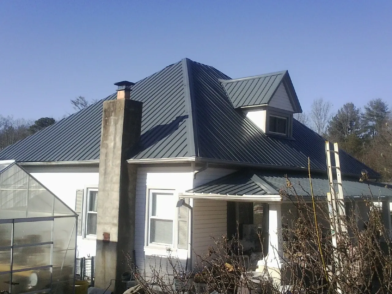 Dark blue standing seam metal roof on a white farmhouse with dormer — Slate & Tile Roof Repair by Roofing Brothers in Morse