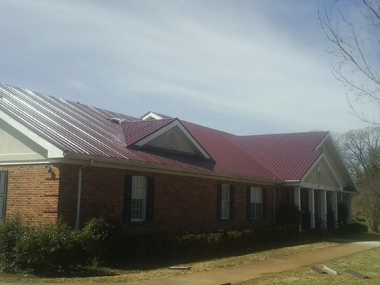 Red metal roof with gabled entries on a long brick building, from a Hail Damage Roof Repair job in Morse