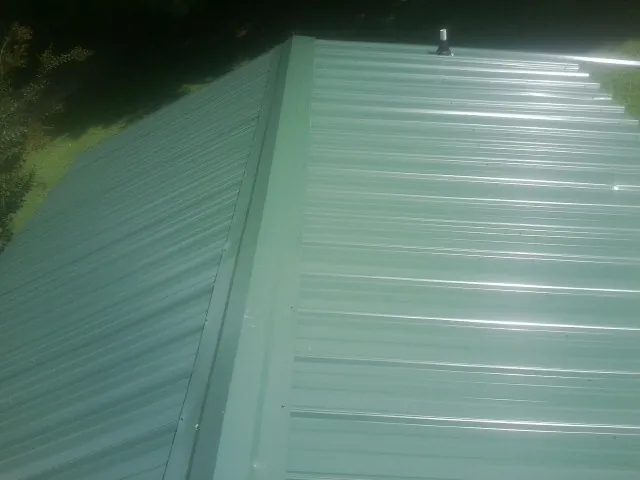 New green metal panels meeting at the ridge of a roof — Flat Roof Repair work by our crew in Morse