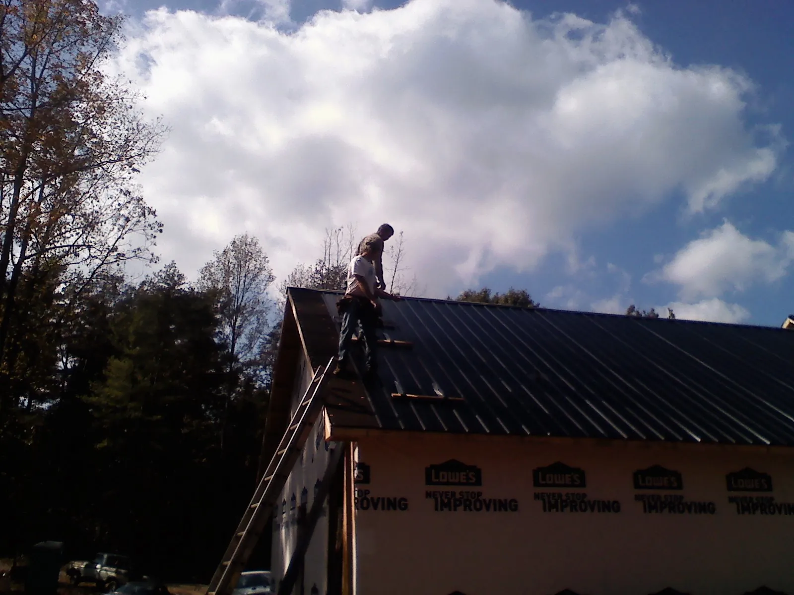Roofer fastening dark metal panels high against a cloudy sky, from a Roof Inspection job in Morse
