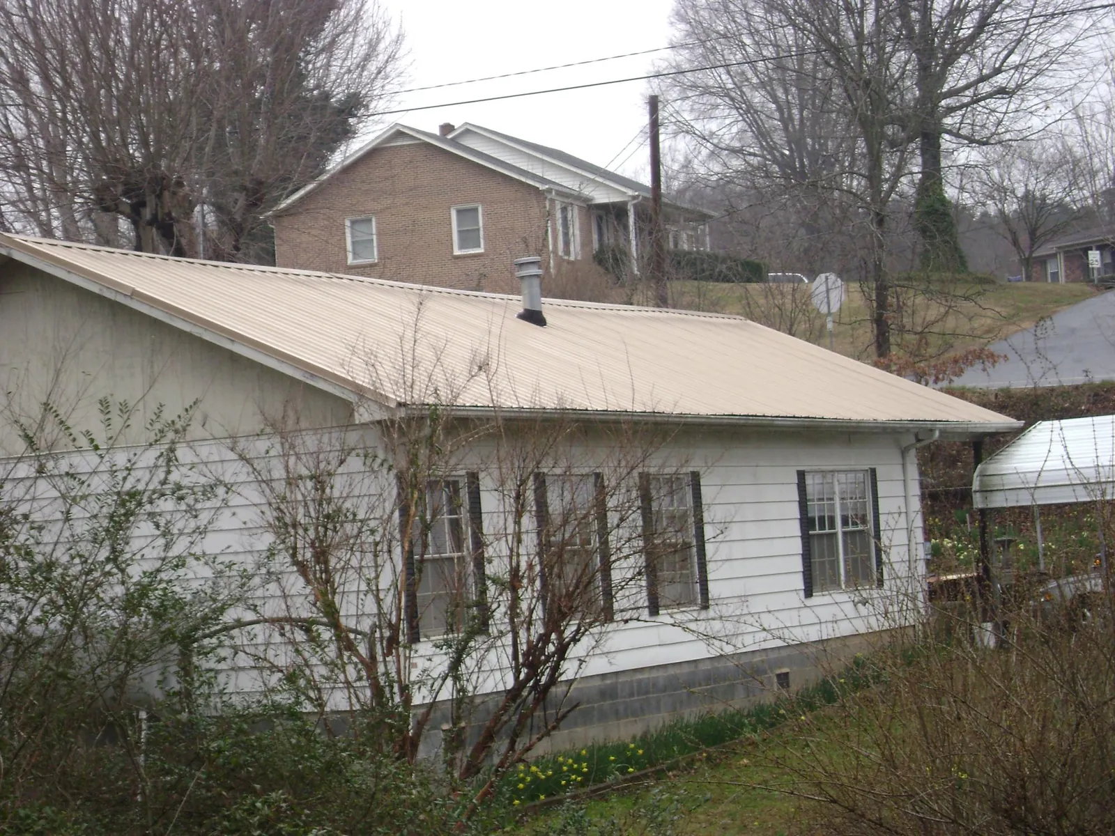 Tan metal roof on a white sided house set into a hillside — Commercial Roofing by Roofing Brothers in Morse