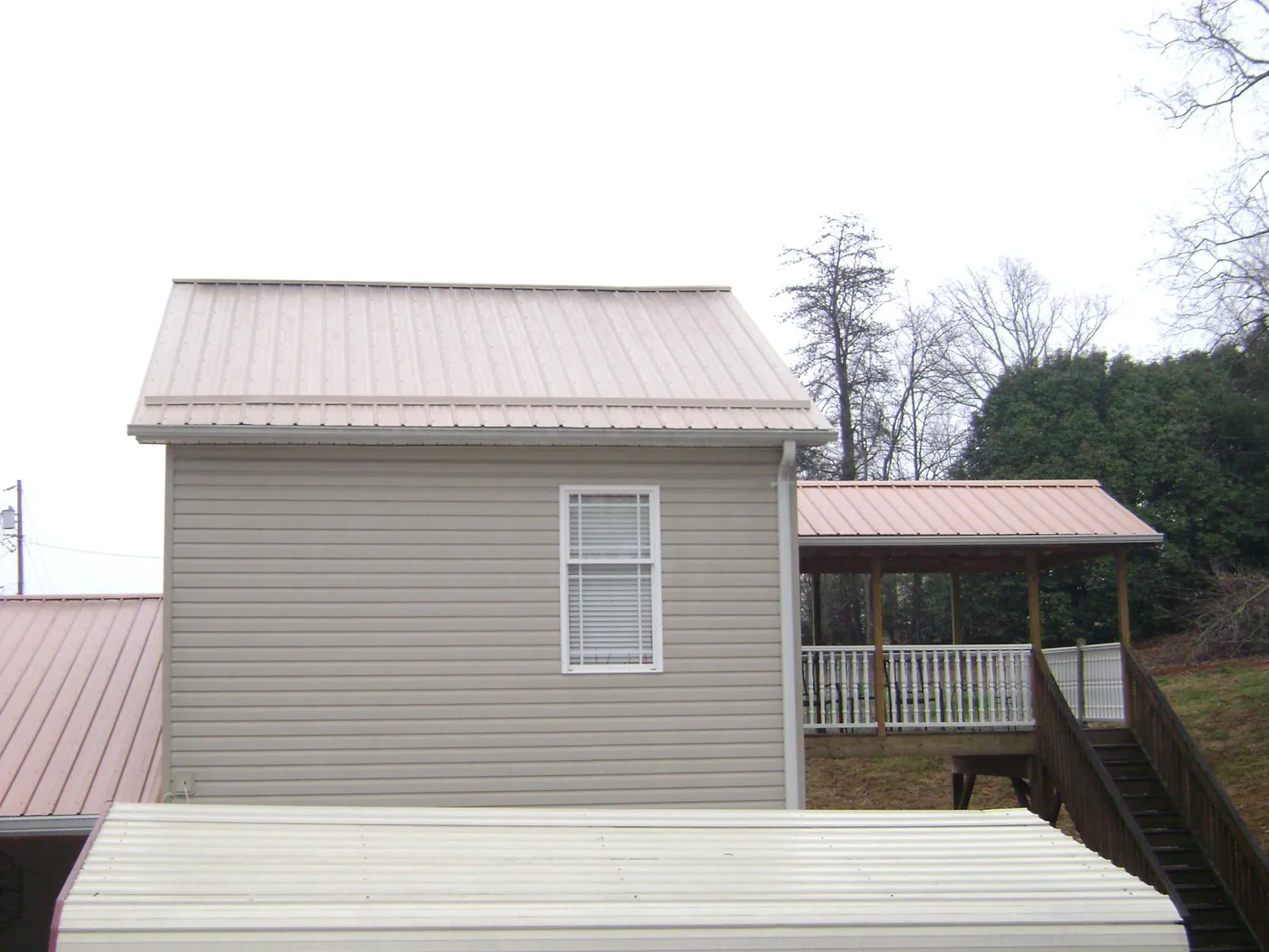 Tan metal roofs on a two story addition and attached porch, from a Roof Replacement job in Morse